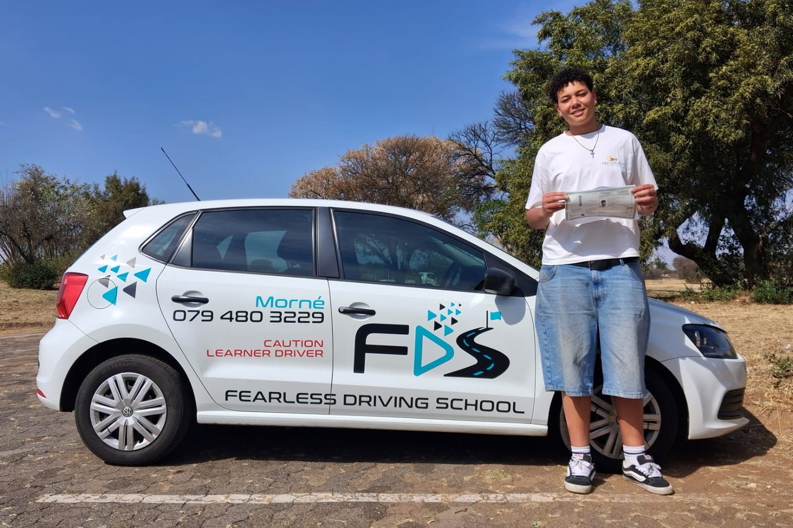 A Fearless learner holding his certificate beside the branded driving-school car